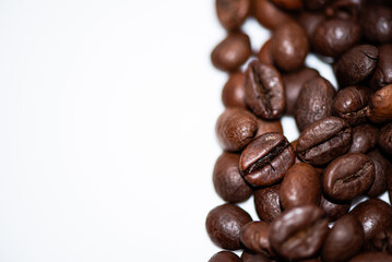 Close-up of rich, roasted coffee beans scattered on a light background, showcasing their glossy surfaces and varying shapes.