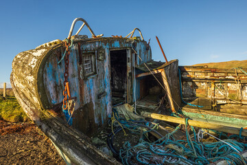 Abandoned and decaying fishing boat wreck blue colored on lakeshore on the Isle of Skye, Scotland,...
