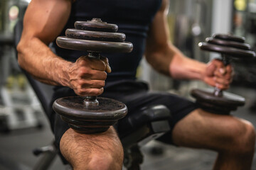 close up on muscular man hold dumbbells and sit on sports bench