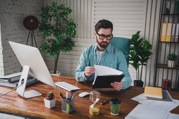 Young professional man working in a home office environment while reviewing documents with focused attention