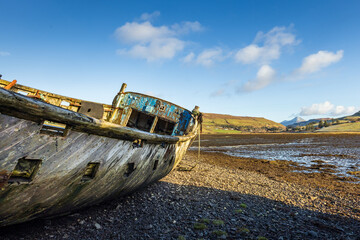 Abandoned and decaying fishing boat wreck blue colored on lakeshore on the Isle of Skye, Scotland,...