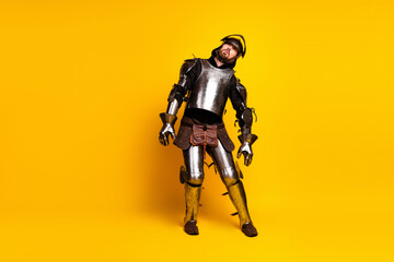 Portrait of a young man dressed as a medieval knight in armor against a vibrant yellow background