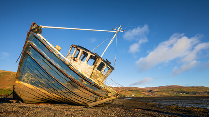 Abandoned and decaying fishing boats wrecks blue colored on lakeshore on the Isle of Skye,...