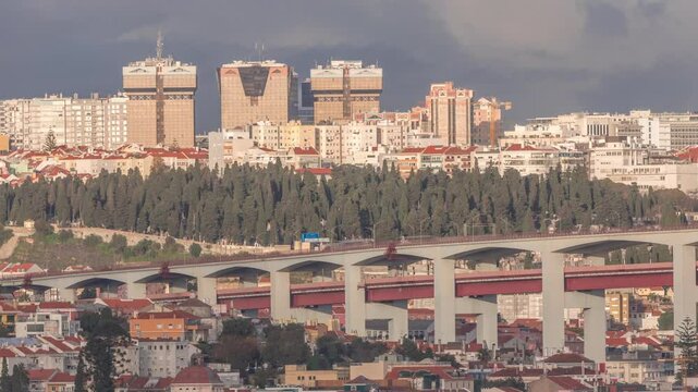 Aerial timelapse of Lisbon skyline featuring colorful houses, Amoreiras shopping center towers and the 25th of April Bridge. Historic district with green trees and Prazeres Cemetery in the foreground