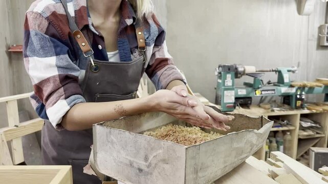 Woodworking Craftsmanship: A focused craftswoman meticulously sifts through wood shavings in her workshop, surrounded by tools and unfinished projects, embodying dedication and skill.