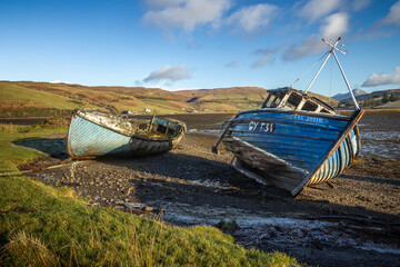Abandoned and decaying fishing boats wrecks blue colored on lakeshore on the Isle of Skye,...