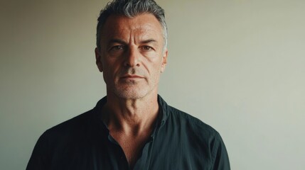 Obraz premium Mature man in dark shirt poses against a neutral beige background exuding calmness and confidence in a portrait session.