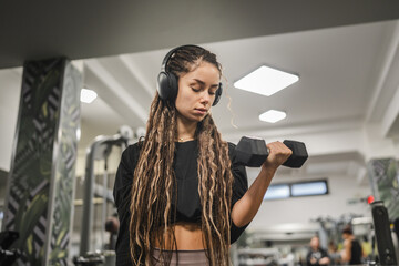 young woman with dumbbells flexing muscles in gym