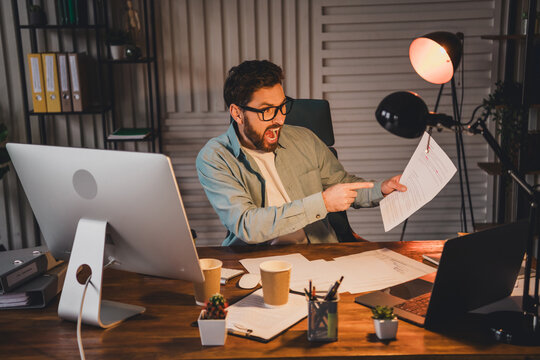Excited professional pointing at document in modern office at night