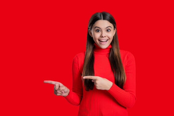 Naklejka premium Teen girl looking at camera. Casual style. Stylish girl has long hair. Teen monochrome fashion style. Style for girl. Headshot portrait of happy teen girl isolated on red. Point finger on copy space