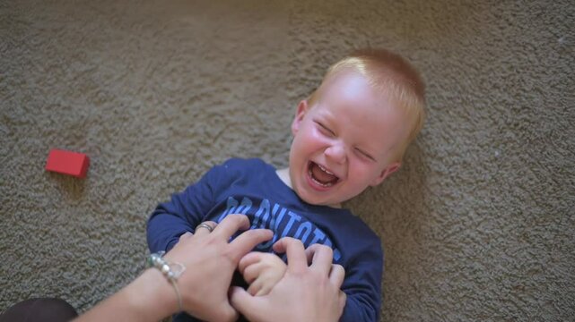 oyful Toddler Laughing During Tickling Playtime toddler laughing uncontrollably while being tickled, enjoying playful and heartwarming bonding moment on soft carpet in cozy home setting