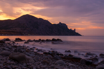 A tranquil beach scene during sunset, with smooth stones scattered along the shoreline. The calm...