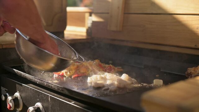 Chef Adding Shrimp to Flat-Top Grill chef preparing shrimp on flat-top grill, placing fresh pieces from colander alongside sauteed vegetables, creating delicious meal in outdoor kitchen