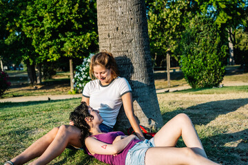 Lesbian couple relaxing under tree in park, embracing love and happiness