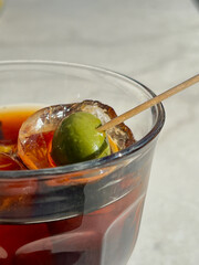 A glass of vermuth during a sunny day. Cocktail in a glass with olive on a tiled table, deep shadows bright light