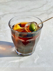 A glass of vermuth during a sunny day. Cocktail in a glass with olive on a tiled table, deep...