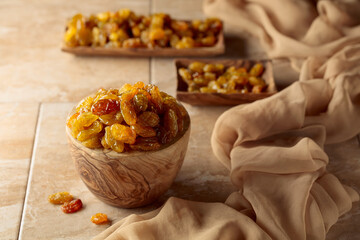 Yellow sultana raisins in a wooden bowl on a beige background.