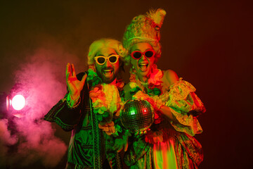 Two people in period costumes enjoying a festive nightclub scene with vibrant colored lighting and...
