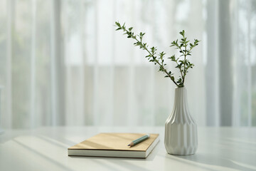 Tall plant vase on white table with notebook by the window, minimal interior, cozy workspace