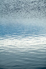 Abstract azure water surface with mild waves, vertical image, reflection of sky