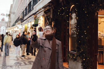 Vlogger traveler woman recording video on phone share via app her travel vacation in the Lisbon. Middle age woman influencer shooting social media stories on the street leading to Commerce Square. UGC