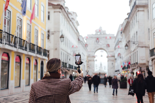 Vlogger traveler woman recording video on phone share via app her travel vacation in the Lisbon. Middle age woman influencer shooting social media stories on the street leading to Commerce Square. UGC