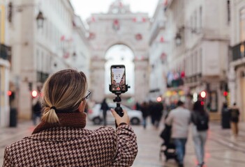 Vlogger traveler woman recording video on phone share via app her travel vacation in the Lisbon. Middle age woman influencer shooting social media stories on the street leading to Commerce Square. UGC