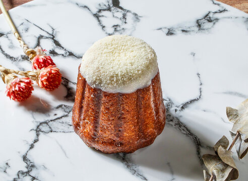 Canele de Bordeaux, a traditional French pastry topped with with powdered sugar isolated on marble background side view of taiwan dessert food
