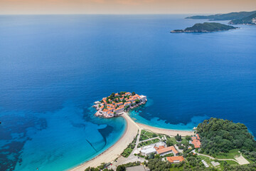 Naklejka premium Aerial view of Montenegro's Sveti Stefan, showcasing its iconic orange rooftops, stunning coastline, and luxurious seaside resort against the beautiful Adriatic Sea.