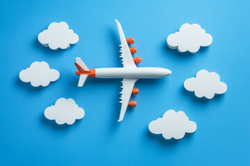 A toy airplane flying through fluffy white clouds on a bright blue background, representing air travel, aviation, and the concept of exploring the sky.