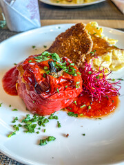 Stuffed Spicy Bell Peppers Rocoto Relleno, salsa, garnish, potato gratin in white plate in restaurant. Colorful Traditional Peruvian Food. high angle view, close up, vertical shot