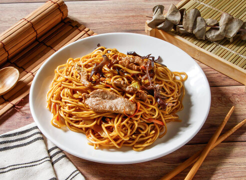 Mu Shu Stir Fried Noodles with Shredded Pork and Vegetables served in plate with chopsticks and spoon isolated on wooden table side view of taiwan food