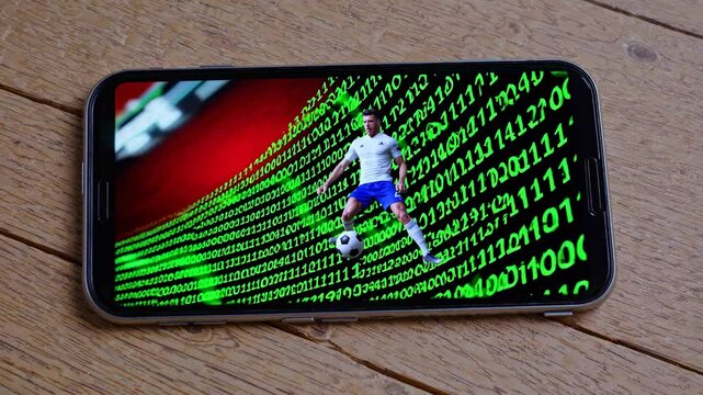 Soccer player kicking a ball is displayed on a smartphone screen, with binary code forming a dynamic backdrop, suggesting online sports betting, virtual reality, or sports technology - Powered by Adobe