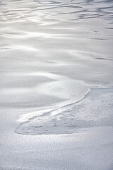 Nature’s artistry is visible in intricate ice fractures on the water surface of the lake