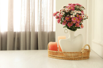 Stylish vase with beautiful flowers and candles on white wooden table at home, space for text