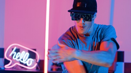 Skilled break dancer wearing fancy glasses with glowing effect while caucasian performer with casual shirt. Close up of skilled man moving to freestyle music and dancing in led light. Regalement.