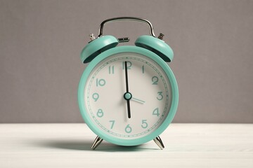 One turquoise alarm clock on white wooden table against grey background