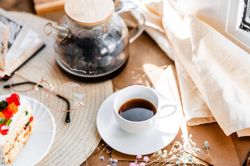 espresso coffee in a white cup on a white saucer on a wooden tray under the sun's rays, a transparent teapot with coffee, flowers, a book, morning coffee, drink, light composition, still life