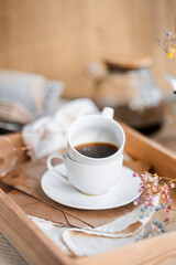 espresso coffee in a white cup on a white saucer on a wooden tray under the sun's rays, a transparent teapot with coffee, flowers, a book, morning coffee, drink, light composition, still life