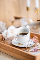 espresso coffee in a white cup on a white saucer on a wooden tray under the sun's rays, a transparent teapot with coffee, flowers, a book, morning coffee, drink, light composition, still life