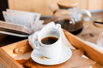 espresso coffee in a white cup on a white saucer on a wooden tray under the sun's rays, a transparent teapot with coffee, flowers, a book, morning coffee, drink, light composition, still life