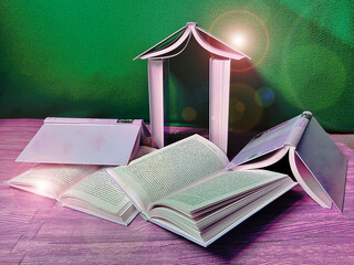 Libros abiertos junto a libro en forma de casa con fondo verde, suelo rosa y reflejo de lente