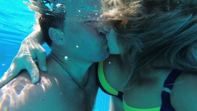 Boy and girl kissing underwater in a pool blowing bubbles