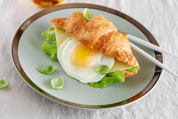 Croissant toast with lettuce, cheese and fried egg on white table. Front view