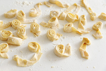 Preparing homemade tagliatelle pasta on on white table: cutted roll of dough. Top view
