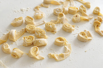Preparing homemade tagliatelle pasta on on white table: cutted roll of dough. Top view