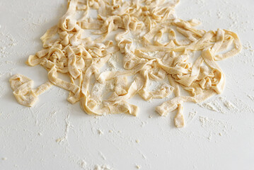 Preparing homemade tagliatelle pasta on on white table: cutted roll of dough. Top view