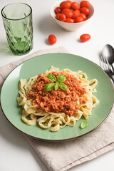 Homemade pasta Tagliatelle Bolognese with meat tomato sauce and fresh basil leaves on green plate. Front view