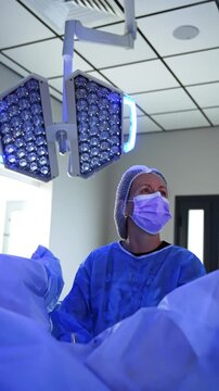 Female surgeon stands at the legs of the patient using endoscopic tool. Doctor looks up at the monitor performing operation. Vertical video.