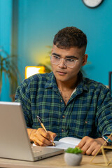 Indian man student freelancer study with notebook write notes making conference video call talking...